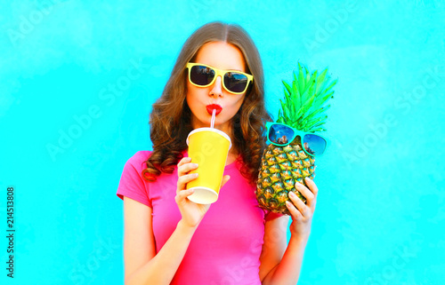 Cool girl holds pineapple drinks juice from cup on a colorful background