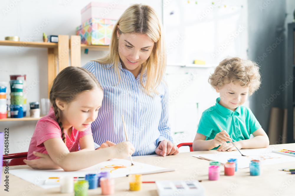 Fototapeta premium Two kids, boy and girl, painting together with their art teacher at the table at art class