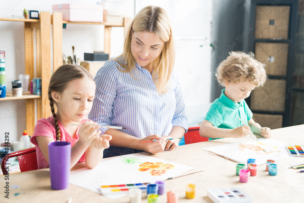 Smiling young teacher drawing with paints and teaching her pupils to paint Smiling young teacher drawing with paints and teaching her pupils to paint