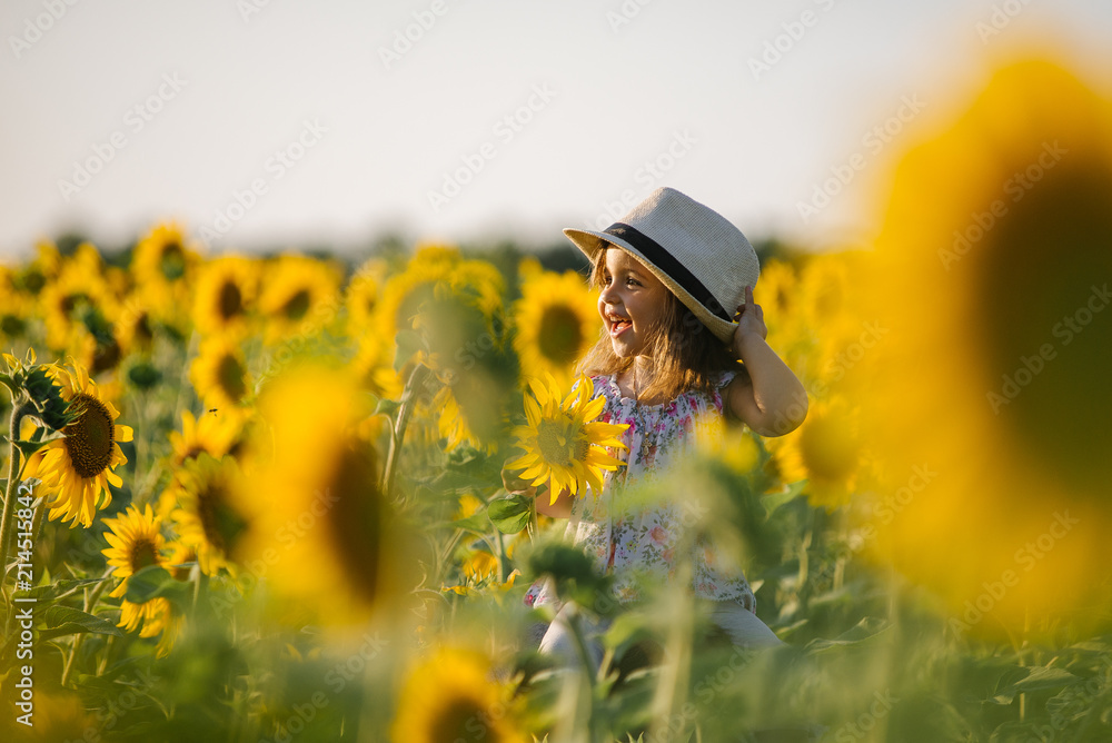 Naklejka premium Happy little girl on the field of sunflowers in summer. beautiful little girl in sunflowers