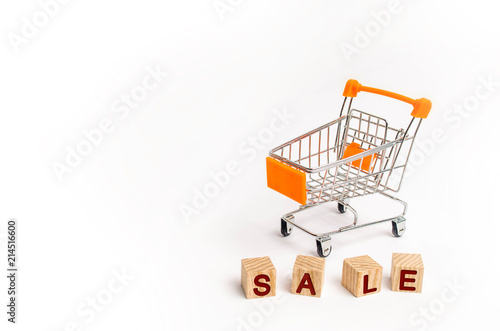 Wooden blocks with the word sale and a supermarket cart on a white background. The concept of sales and seasonal sales of goods and services. Discounts and promotions. Place for text.