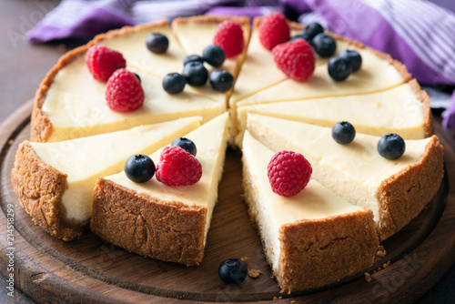 Classic plain New York Cheesecake with fresh berries sliced on wooden board. Closeup view