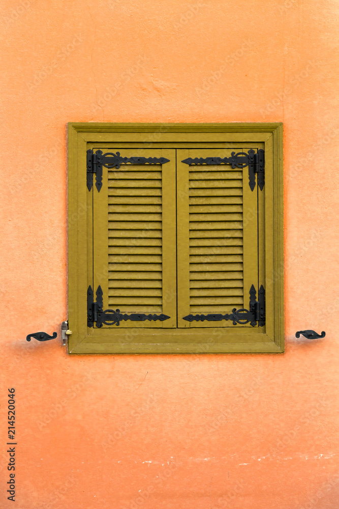 Old window with green wooden shutters on a vivid orange wall, closeup background.