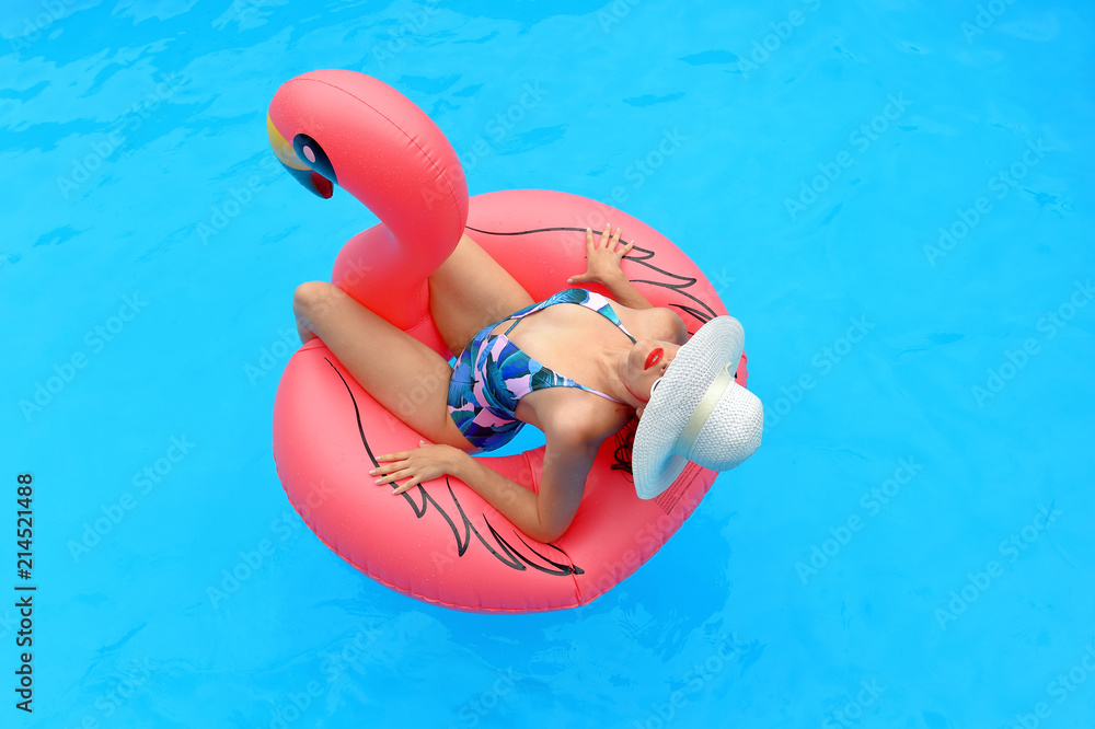 A young woman wearing a bathing suit and  a white summer hat sits relaxed in an  inflatable swim ring. 