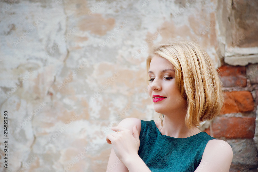 A blonde girl in a stylish green overalls hugs herself against a background  of an old brick wall close-up. A woman's portrait on the street. Stock  Photo | Adobe Stock
