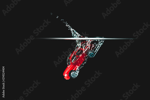 A red car hits the water, black background. Toy car, vehicle dropping in water and creating a splash. Toy thrown into the water, road accident, the effect of the car's fall. photo