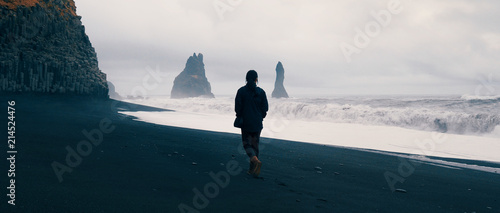 Woman walking alone on black sand beach at Reynisfjara, Iceland. 