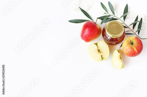 Rosh hashana, Jewish New Year greeting card, invitation. Food styled stock composition with honey jar, apples, olive branch and ribbon isolated on white table background. Flat lay, top view.