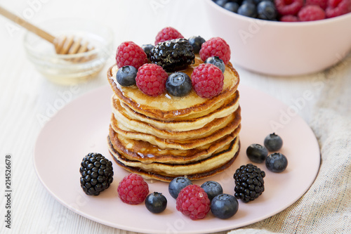 Delicious pancakes with berries and honey on a pink plate, side view. Closeup.