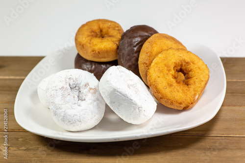 An assortment of donuts, powder donuts, chocolate donuts and plain donuts and a table waiting to be eaten