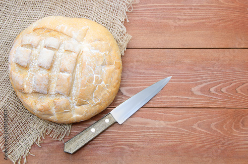 A loaf of wheat bread and a knife. On a brown wooden background.