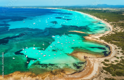 Aerial view of transparent sea with blue water, sandy beach, rocks, green trees, yachts and boats in sunny morning in summer. Travel in Mallorca, Balearic islands, Spain. Top view. Colorful landscape