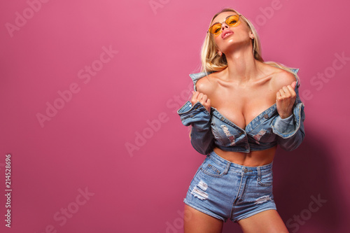 Portrait of young beautiful fit and sexy blonde woman on pink background in studio wearing sunglasses. Fashion concept