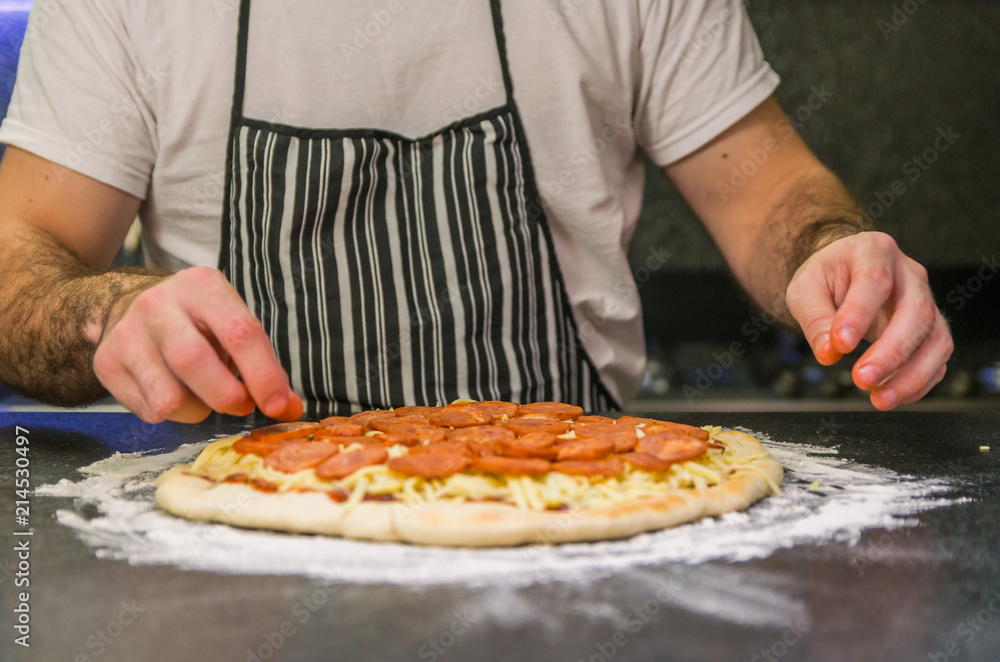 Man preparing pepperoni pizza on black granite table Man preparing pepperoni pizza on black granite table