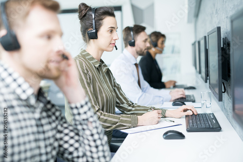 Εκτύπωση καμβά Side view portrait of several help desk operators wearing headsets sitting in ro