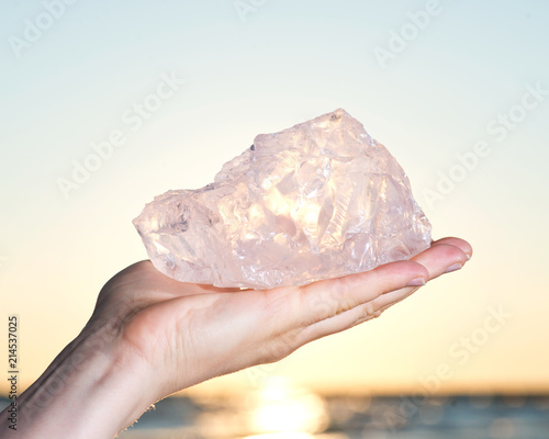 Woman's hand holding gem grade rough Rose Quartz chunk from Madagascar  in front of the lake at sunrise photo
