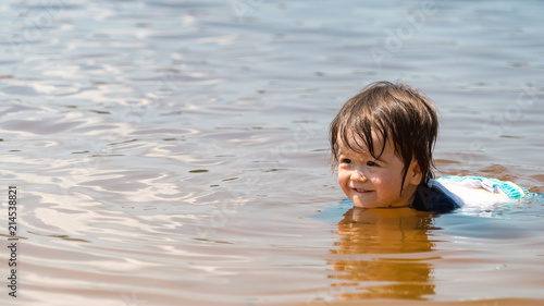 Toddler boy swimming in a big lake on a summer day