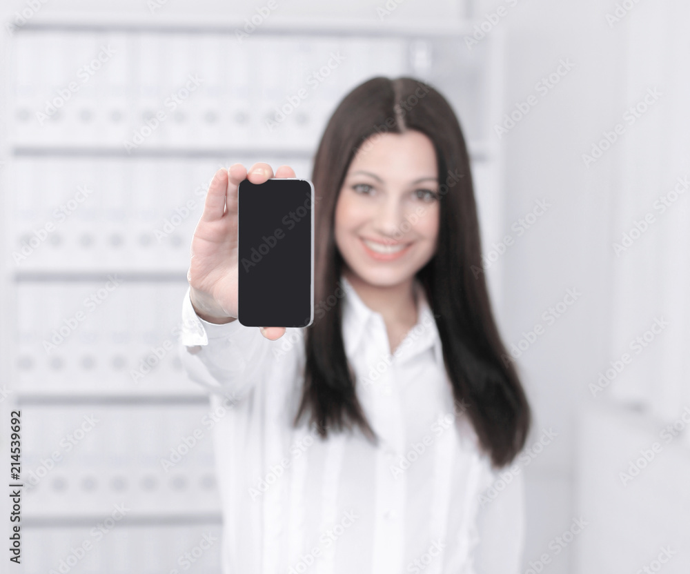 smiling female assistant showing a mobile phone standing in office. smiling female assistant showing a mobile phone standing in office.