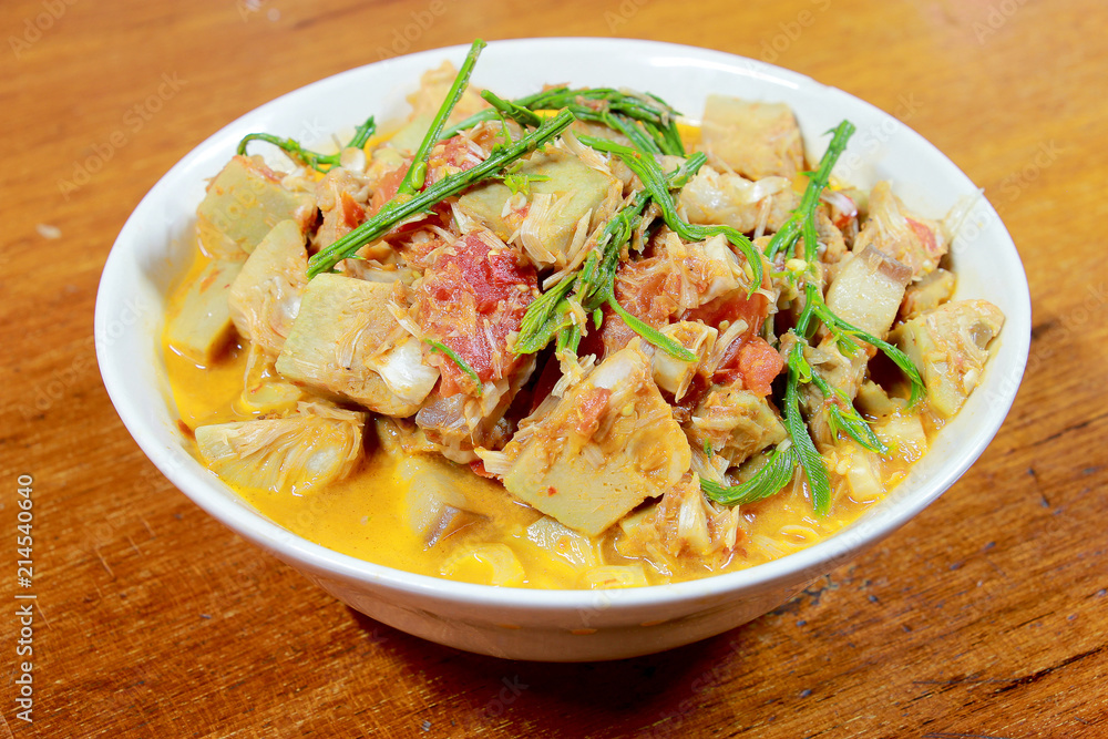 Northern Thailand local food called Kaeng Khanun-on is cooking like a young jack fruit soup with pork spare rib Thai herb, Climbing Wattle, Acacia pennata, red eggplant in white bowl on wooden table. Northern Thailand local food called Kaeng Khanun-on is cooking like a young jack fruit soup with pork spare rib Thai herb, Climbing Wattle, Acacia pennata, red eggplant in white bowl on wooden table.