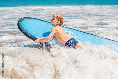 Happy baby boy - young surfer ride on surfboard with fun on sea waves. Active family lifestyle, kids outdoor water sport lessons and swimming activity in surf camp. Summer vacation with child photo