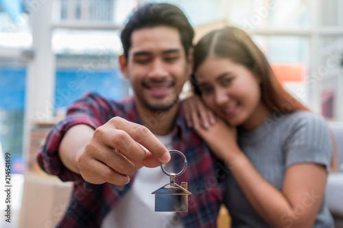 Closeup Asian young couple holding the house key chain in Love and glad feeling after successfull packing the big cardboard box for moving in new house, Moving and House Hunting concept, photo