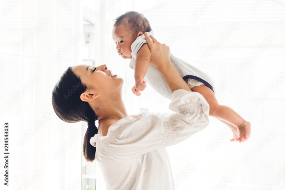 Fototapeta premium Portrait of happy smiling mother playing with baby on bedroom at home.Love of family concept
