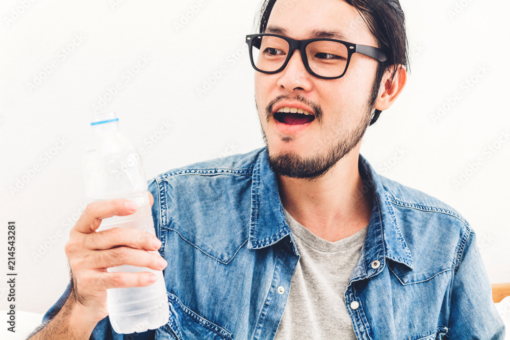 Healthy young man drinking water from a bottle while relaxing and feeling fresh at home Healthy young man drinking water from a bottle while relaxing and feeling fresh at home