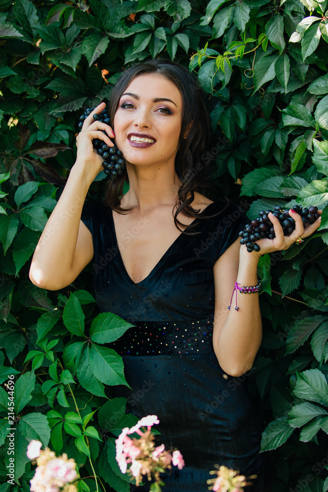 Portrait of young sexy brunette with black grapes.
