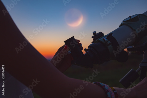 Girl looking at lunar eclipse through a telescope.  photo