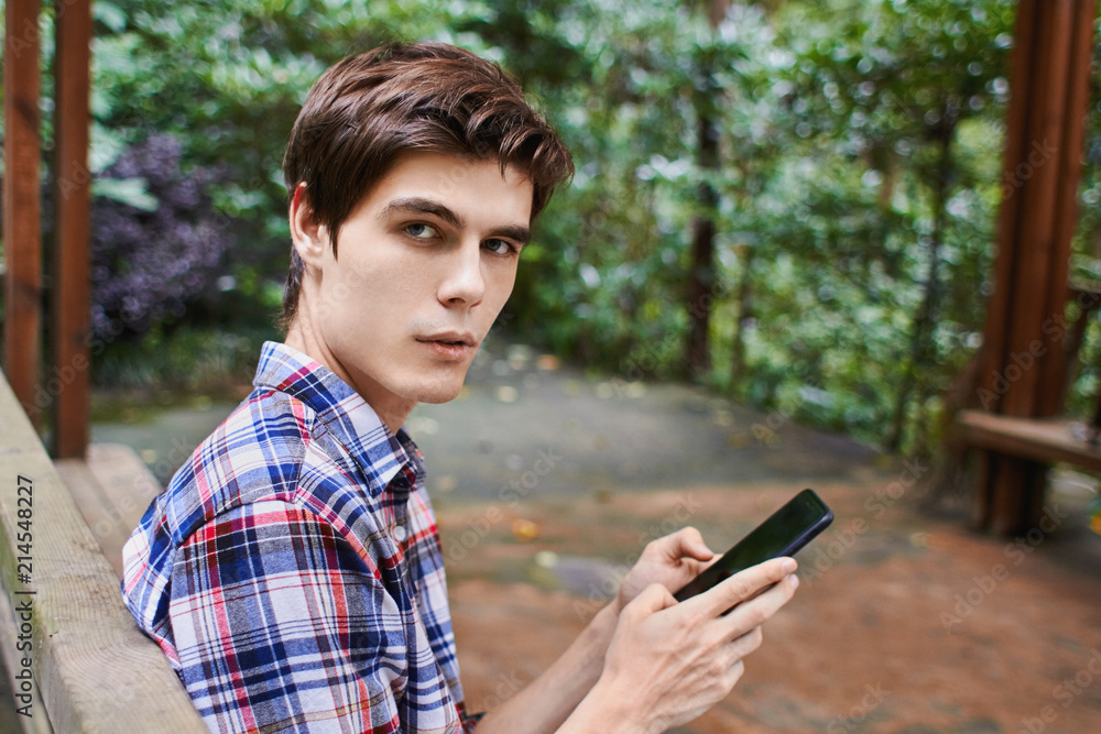 Man is sitting in the wooden pavilion and looking at the cellphone in the forest Man is sitting in the wooden pavilion and looking at the cellphone in the forest