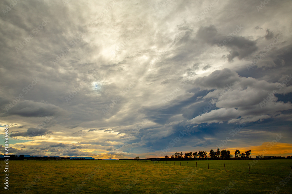 Naklejka premium Storm clouds gather overhead and bright light filters through the gaps to the fields below