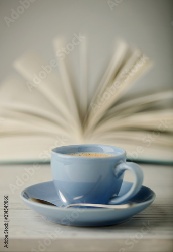 Coffee in a light blue cup and book in blue cover on a wooden background.