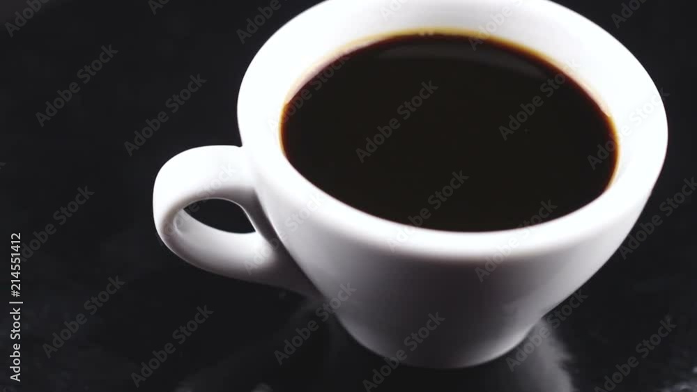 Black coffee in white cup rotating on dark surface. Black coffee in white cup rotating on dark surface.