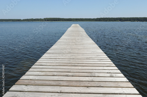 wooden pier flows into the blue water of the lake in summer