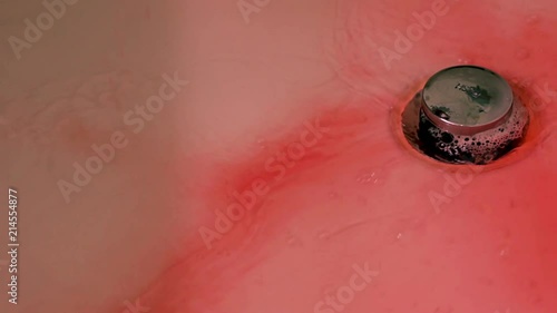 Red blood being washed down a white bathtub drain.  Horror movie concept of bright red blood being cleaned up and going down the drain.