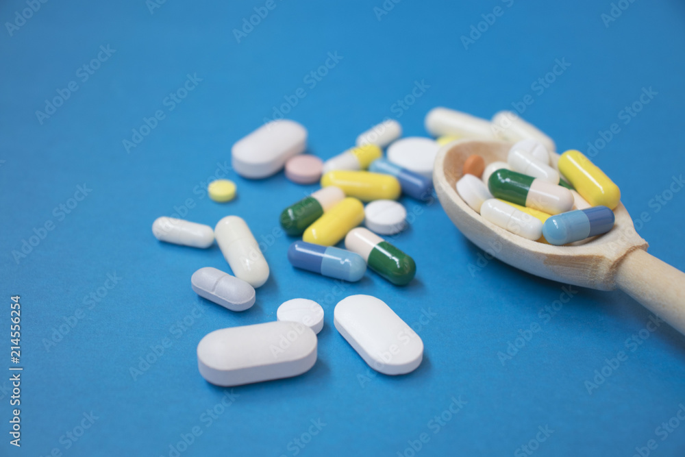 Colorful tablets and pills in wooden spoon. Pharmaceutical pills in wooden spoon on blue background. copy space Colorful tablets and pills in wooden spoon. Pharmaceutical pills in wooden spoon on blue background. copy space