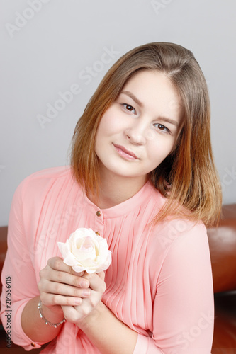 Cute girl teenager in pink dress sits with white rose in studio
