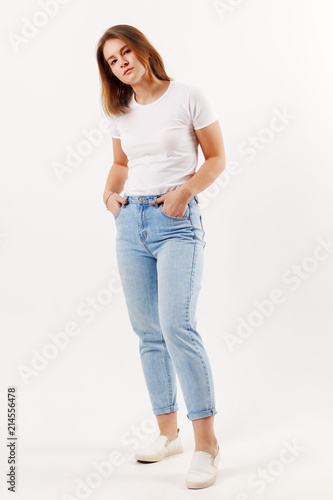 Beautiful happy girl teenager in white t-shirt and jeans poses in white studio