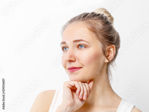 Pretty young girl with make-up props up chin and looks away in studio, close up portrait