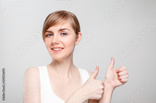 Beautiful young woman with make-up thumbs up and smiles in studio