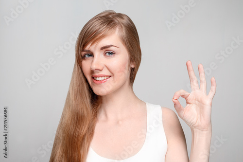 Beautiful young woman with make-up shows Ok gesture and smiles in studio