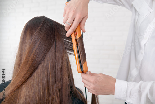 Valokuva Hairstylist working with client brown hair, keeping straightener, making curles