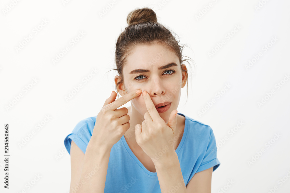 Those nasty acne came again. Portrait of intense focused gloomy cute woman with bun hairstyle, bending towards camera as if looking in mirror, squeezing skin with fingers to get rid of pimple Those nasty acne came again. Portrait of intense focused gloomy cute woman with bun hairstyle, bending towards camera as if looking in mirror, squeezing skin with fingers to get rid of pimple
