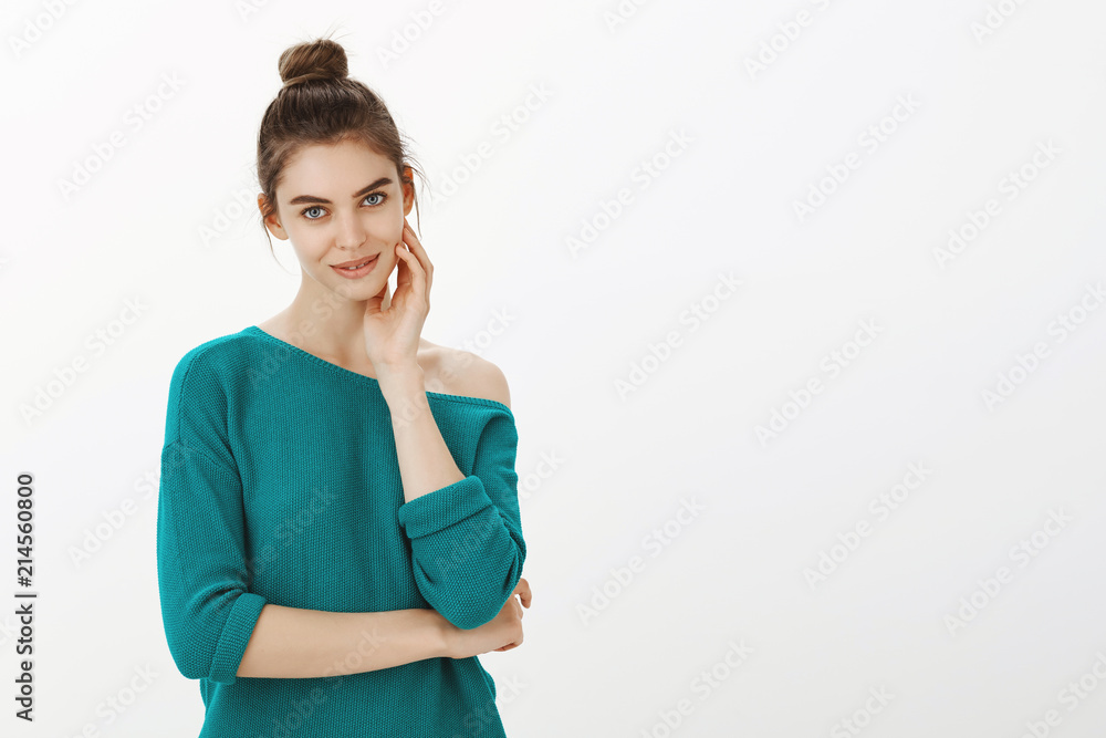Portrait of intriguing feminine woman with bun hairstyle in green loose sweater, gently touching face and gazing at camera with sensual and cute smile, hinting at something or looking passionately Portrait of intriguing feminine woman with bun hairstyle in green loose sweater, gently touching face and gazing at camera with sensual and cute smile, hinting at something or looking passionately