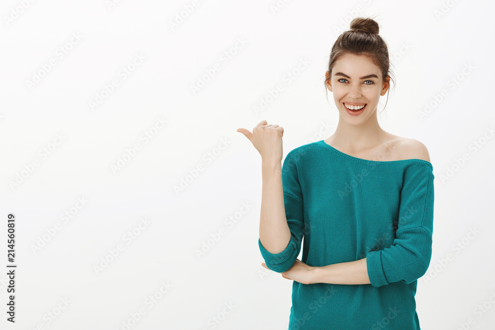 You should ask that guy. Portrait of carefree emotive beautiful woman with bun hairstyle in green loose sweater, pointing left with thumb and smiling joyfully while discussing something awesome You should ask that guy. Portrait of carefree emotive beautiful woman with bun hairstyle in green loose sweater, pointing left with thumb and smiling joyfully while discussing something awesome