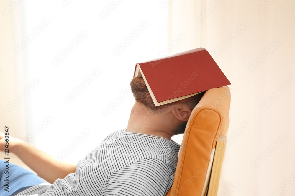 Obraz premium Young man sleeping with book on his face at home