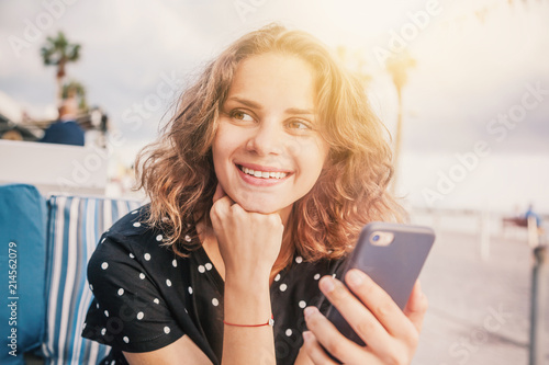 Young beautiful happy smiling woman with a smartphone in hands sitting in a street cafe, close-up portrait, shot of a head photo