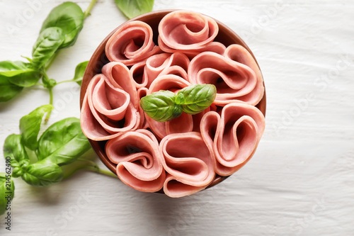 Fotografija Bowl with delicious sliced and rolled ham on wooden table, top view