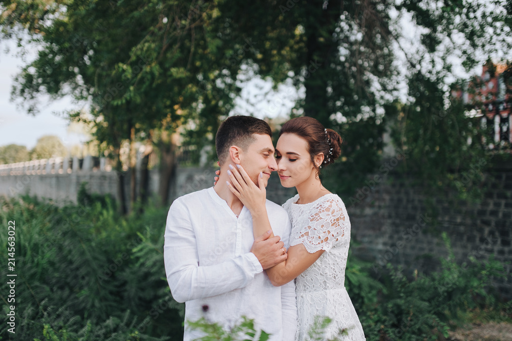 Beautiful newlyweds hugging against a background of green foliage. A stylish bridegroom smiles at the cute bride. Wedding portrait. Beautiful newlyweds hugging against a background of green foliage. A stylish bridegroom smiles at the cute bride. Wedding portrait.
