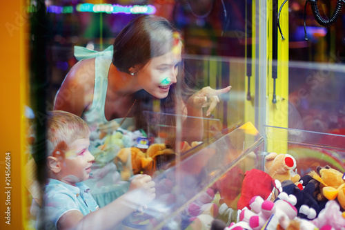 Cute boy in blue t-shirt with him young mother plays arcade in game machine at an amusement park.